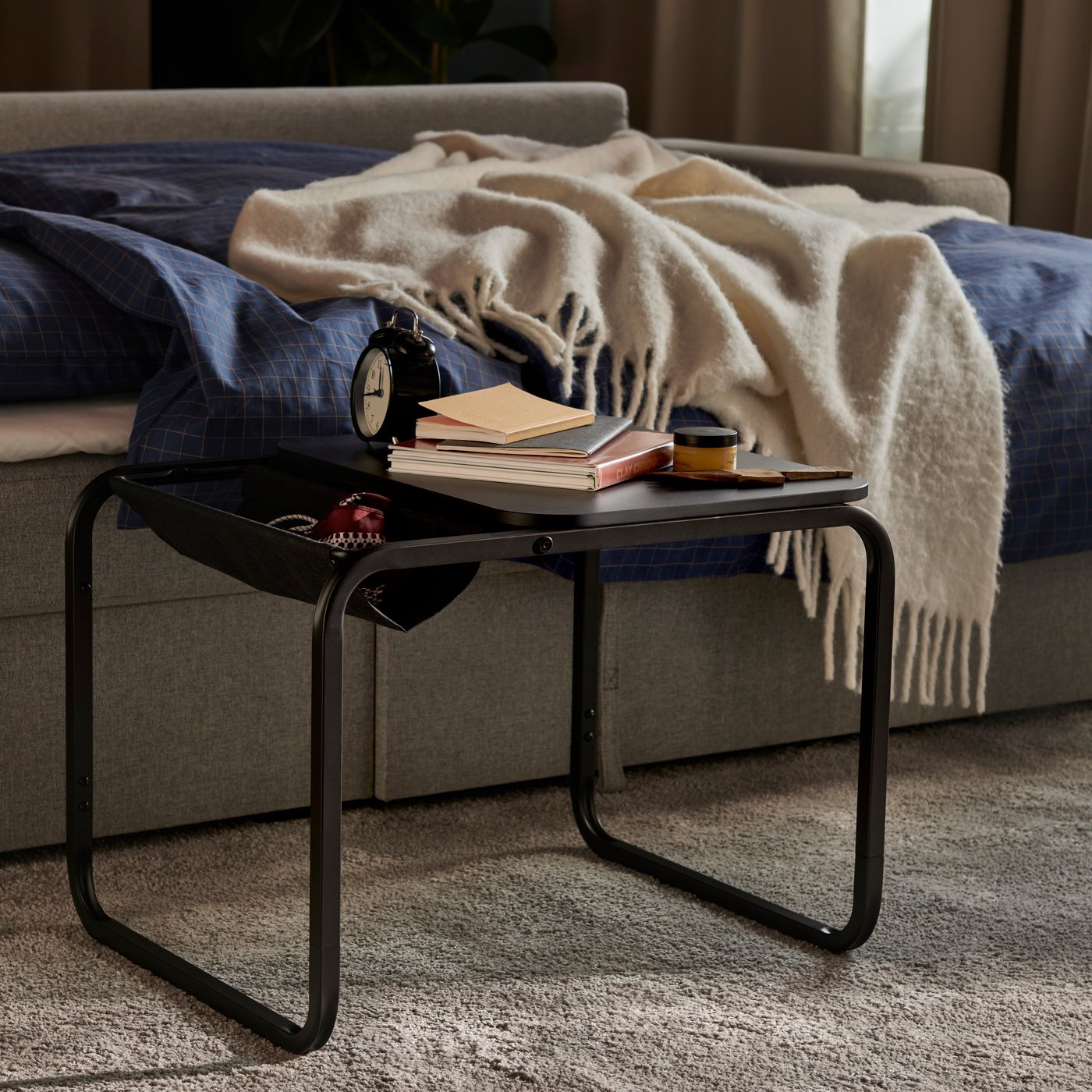 A beige/grey BÅRSLÖV three-seat sofa-bed with a chaise longue, draped with a cosy blanket and placed beside a side table.