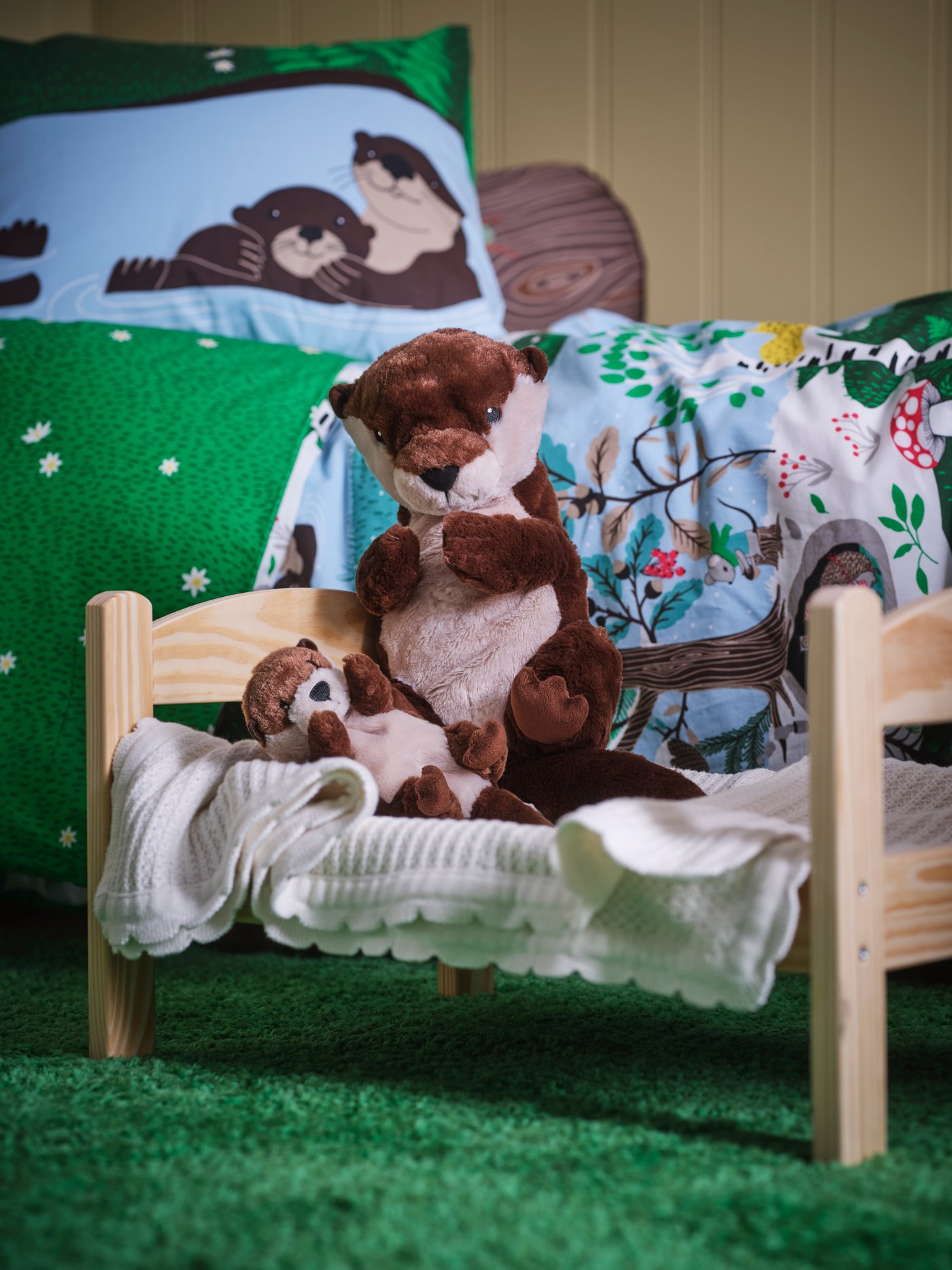 Peluche de nutria SKOGSDUVA sobre cama de madera infantil con ropa de cama infantil.
