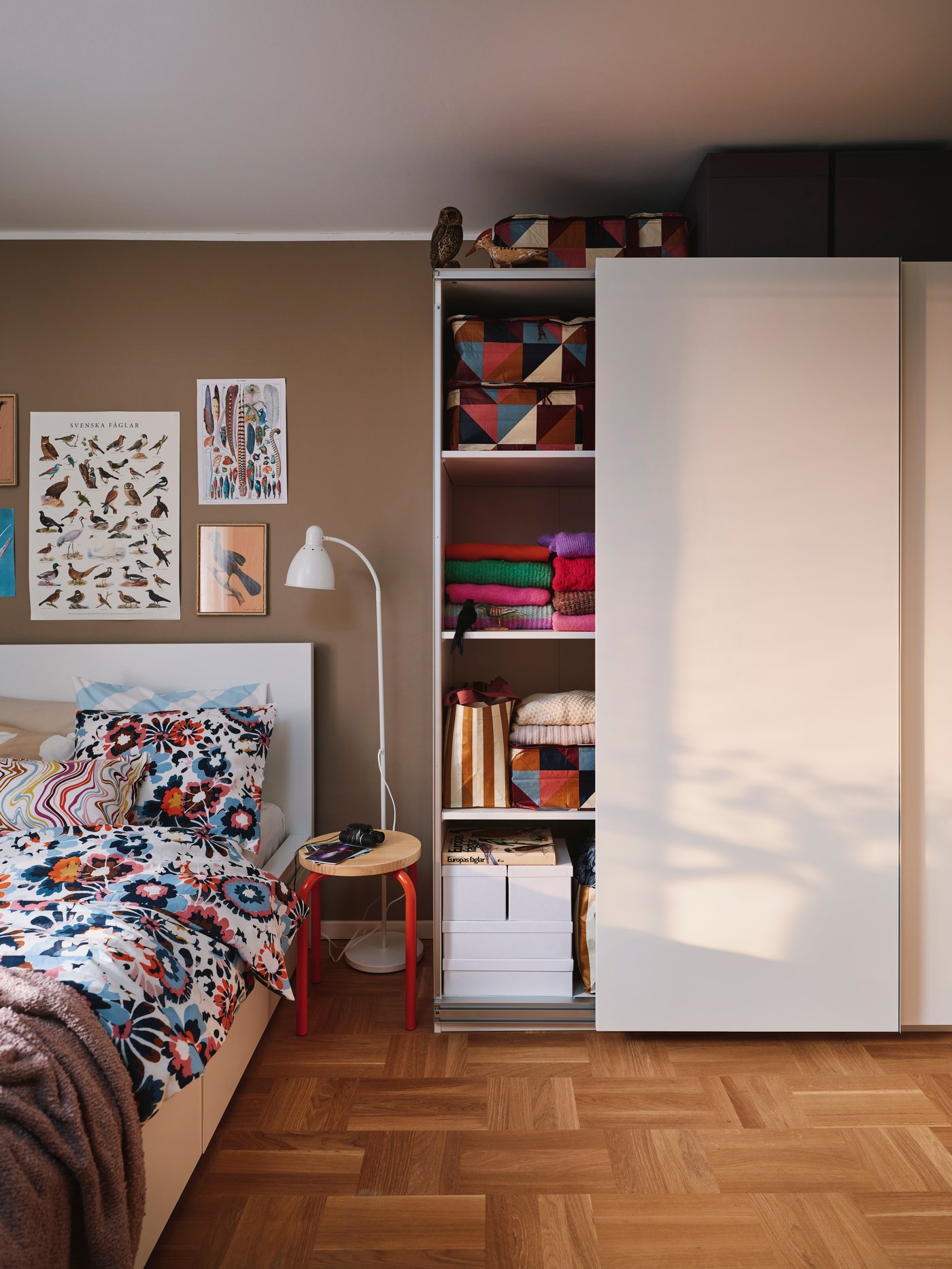 En vit PAX garderob i ett ljust sovrum med färgglada detaljer.