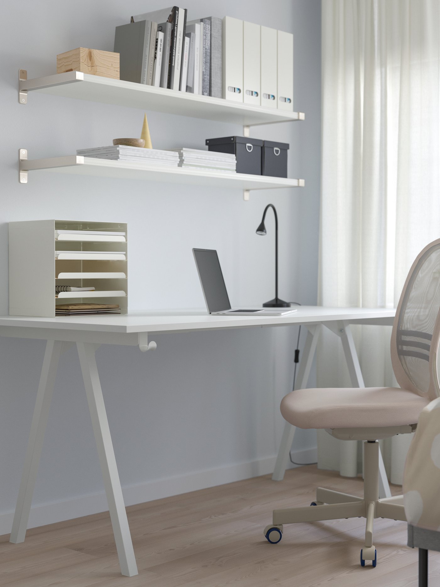 Scrivania TROTTEN bianca con cavalletti in un angolo studio luminoso, completata da sedia girevole e mensole con libri e contenitori sopra.