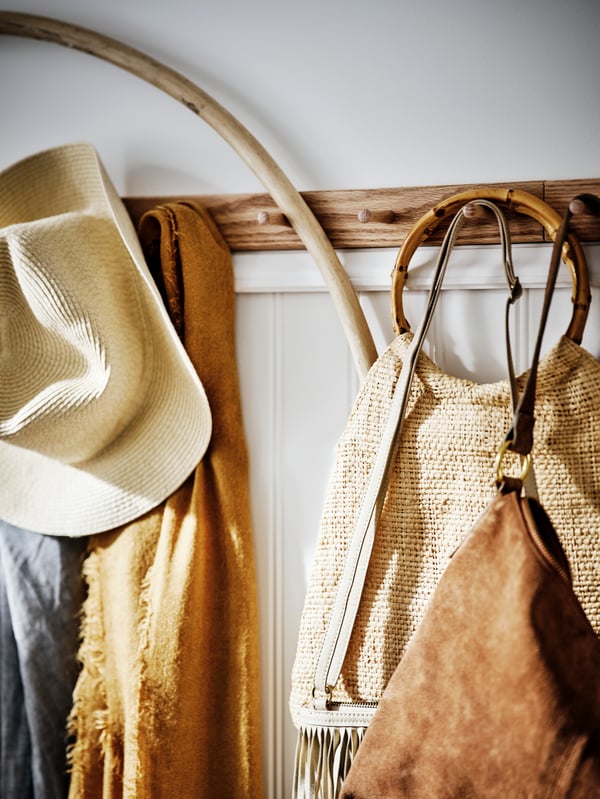 Perchero de madera instalado en la pared con un sombrero, bufanda y bolsas colgados.