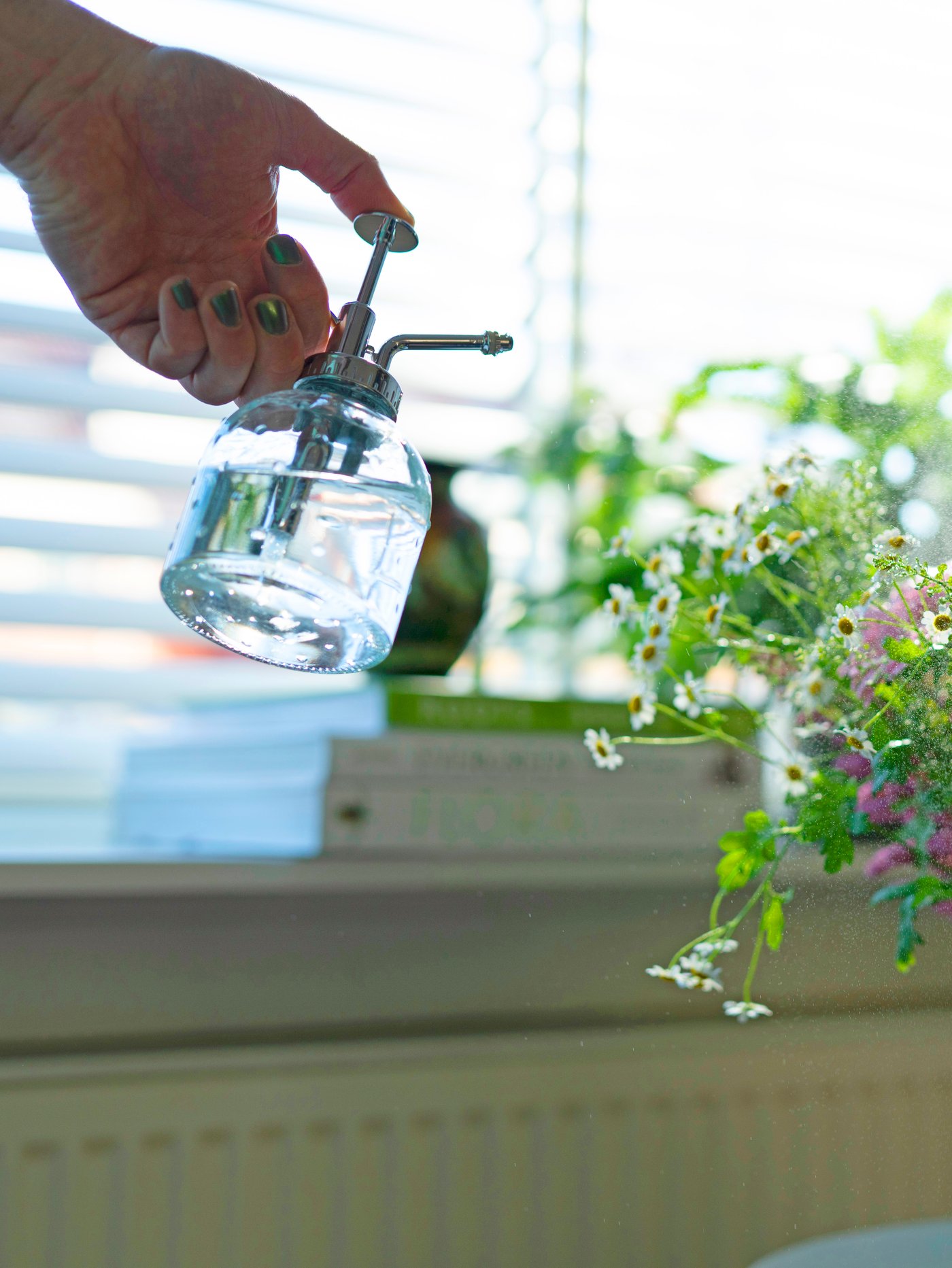 A hand uses a SESAMFRÖN plant mister to spray water mist on fresh flowers in a BERÄKNA vase.