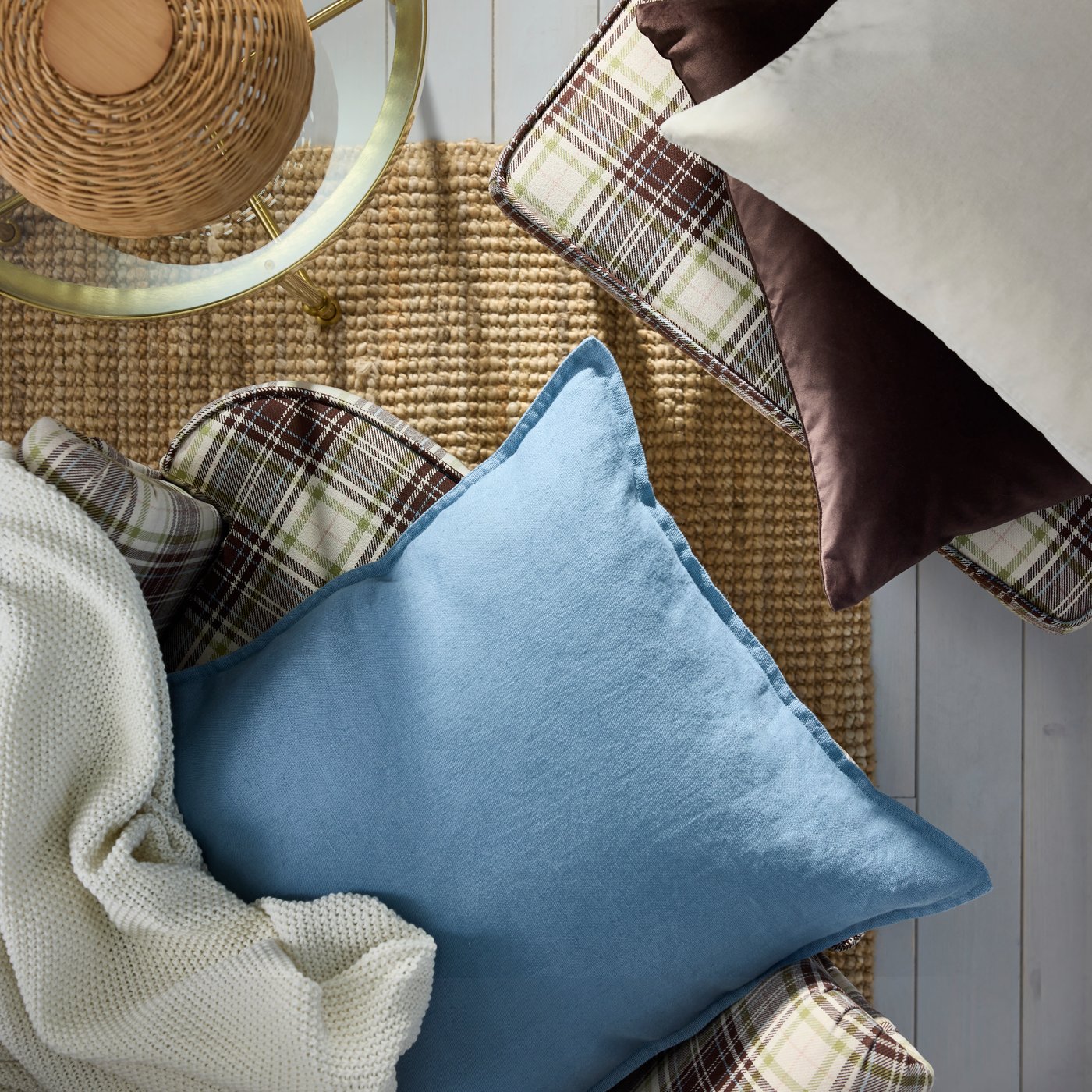A cushion and throw on a softly sunlit tartan-pattern, beige-brown STRANDMON wing chair and footstool by a TORSJÖ side table.