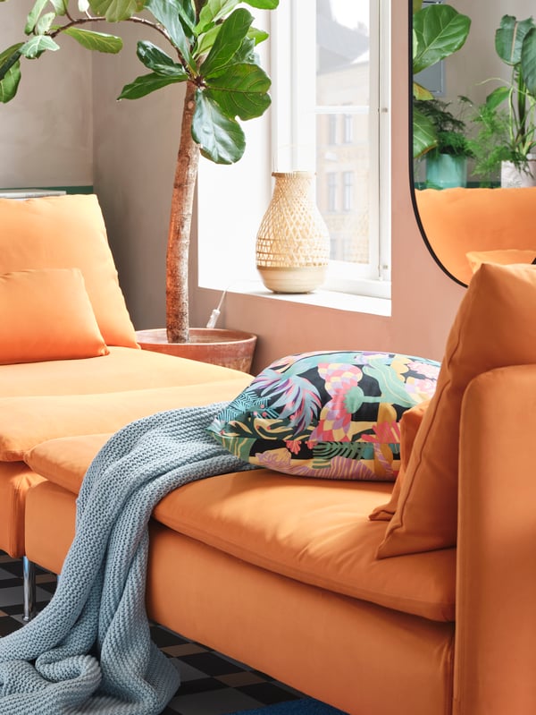 Two orange chaise longues pushed together to create a day-bed, with a blue throw and a colourful floral cushion on top.