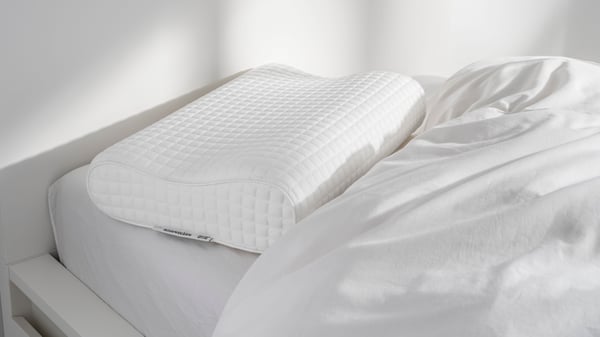 Valkoinen ROSENSKÄRM-ergotyyny on valkoisella petaamattomalla sängyllä.