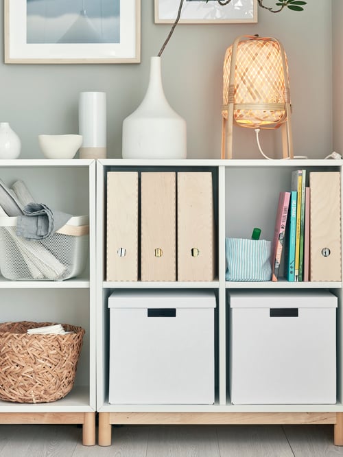 Living room with cabinets with compartments, boxes with lids, magazine files, table lamp, basket, candle, frames on the wall.