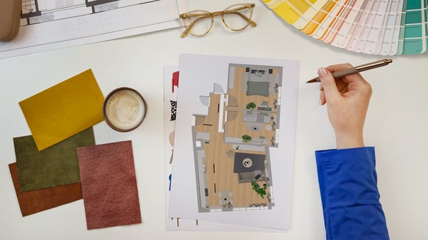 Biurko, na którym leżą probki materiałów, kartki z rzutami pomieszczenia, wzornik kolorów i ręka projektantki IKEA.