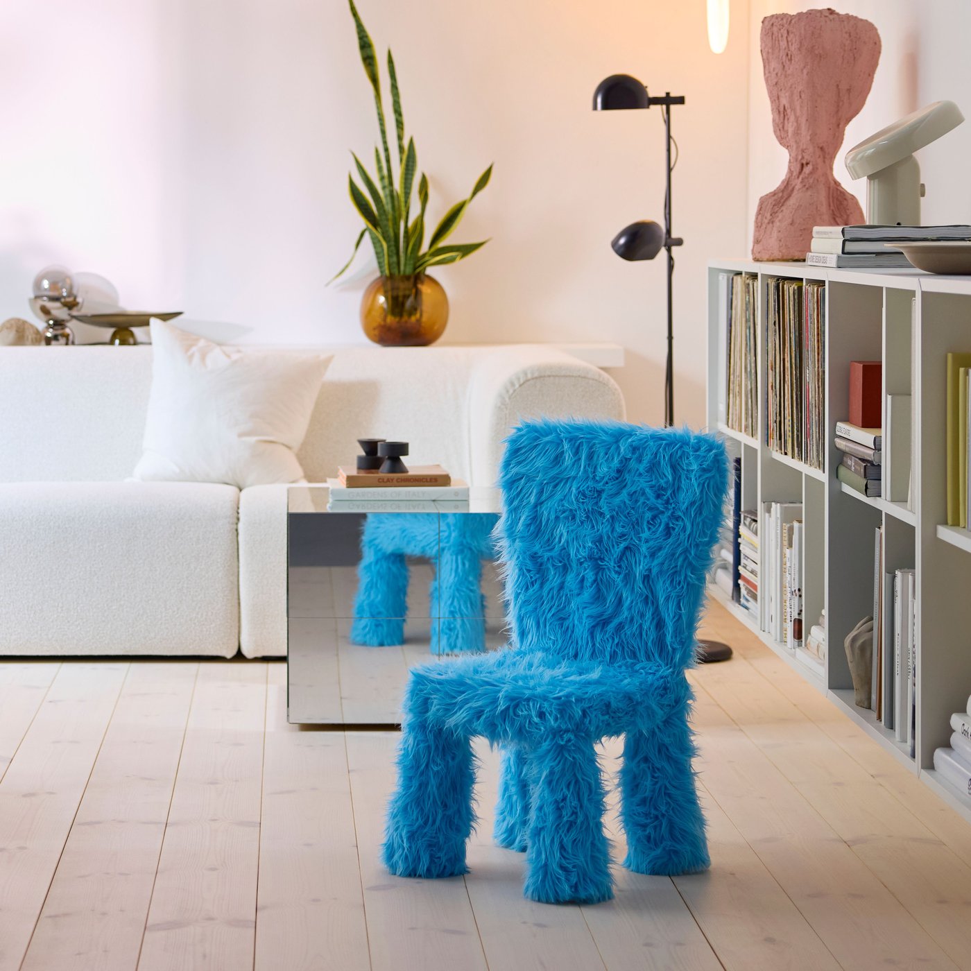 A child’s chair in a GRESIMOJS chair cover in blue faux fur is in a bright and modern living room, by a mirrored side table.