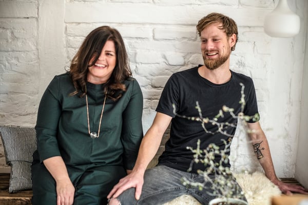 A couple sitting on a bench against an interior brick wall. 