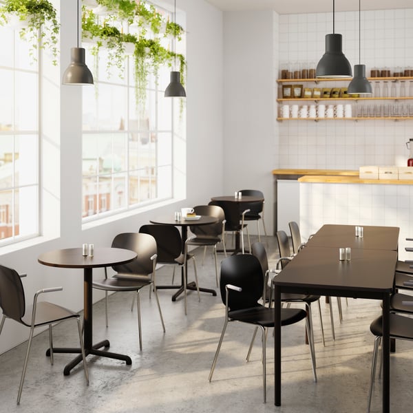 A lunchroom with different sized tables and chairs and black HEKTAR lamps hanging above.
