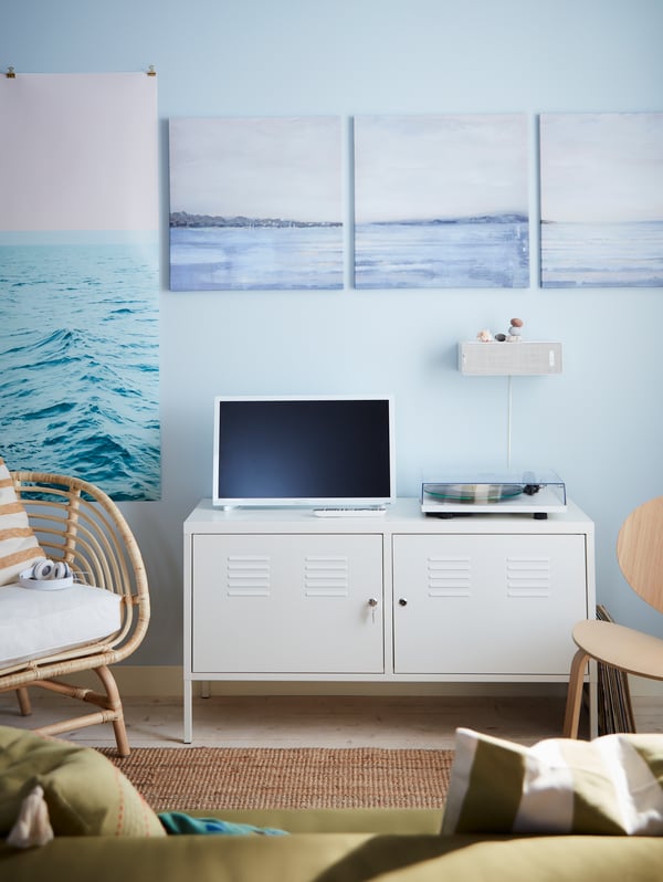 A white cabinet with a TV and record player on top, against a blue wall with prints featuring the sea.