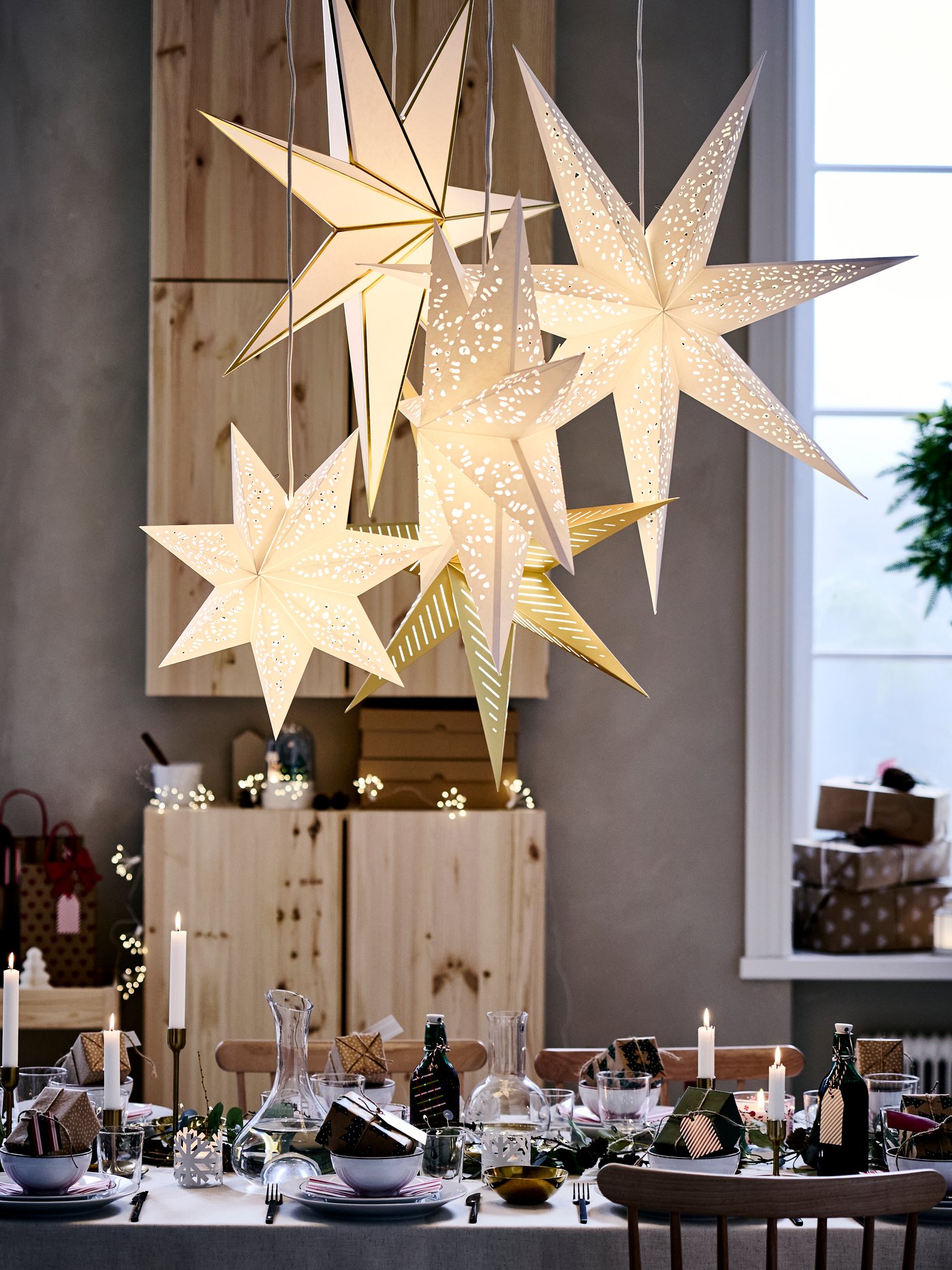Festligt dukat bord med ljus, paket och hängande stjärnlyktor i ett julpyntat rum.