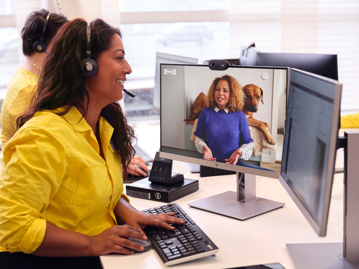 Un/a compañero/a de IKEA tiene un auricular con una camisa amarilla y está hablando con una persona que confía en IKEA de forma virtual en la computadora.