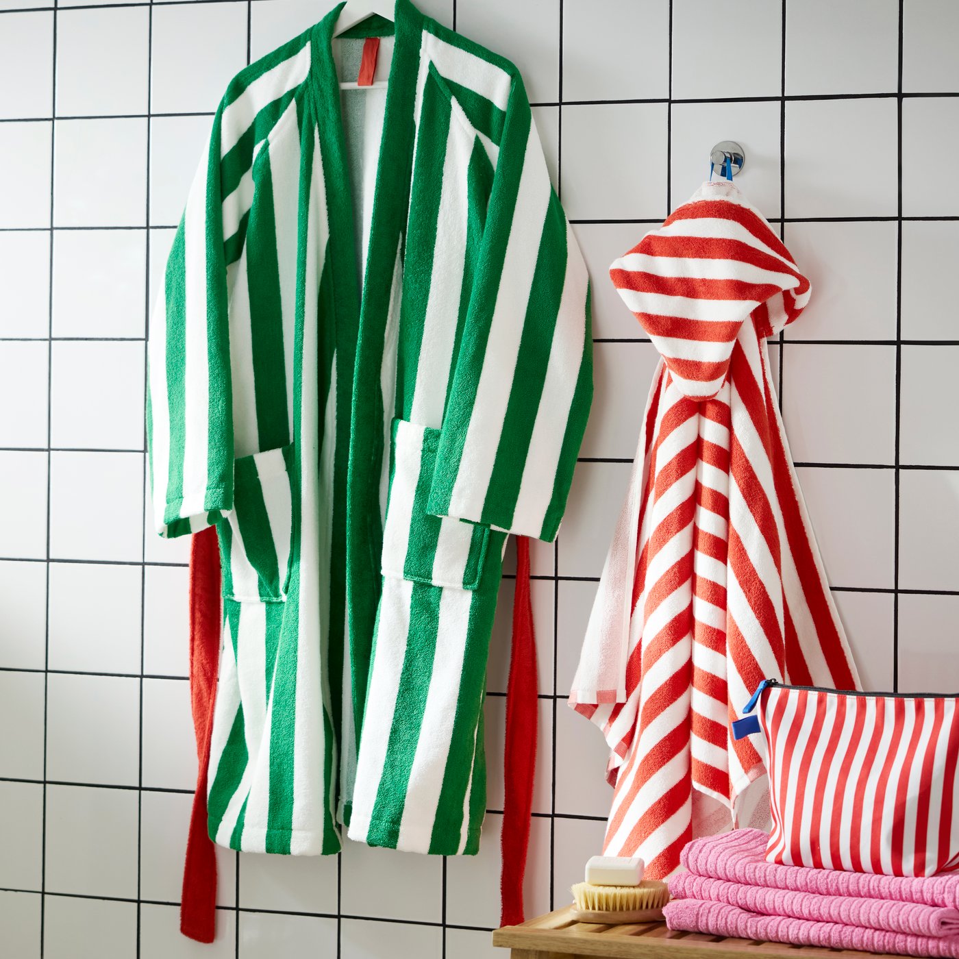 A large SKOGSSALLAT bathrobe with green and white stripes hanging on a white wall next to a small poncho with red stripes.
