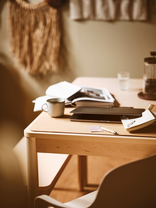 A dining area with a grey GLADELIG mug, a cork SUSIG desk pad, and a laptop placed on a RÖNNINGE extendable table.