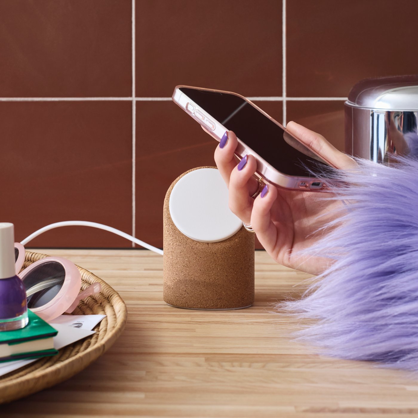 A person’s hand places a mobile phone on a VÄSTMÄRKE wireless charging stand which is placed on a worktop.