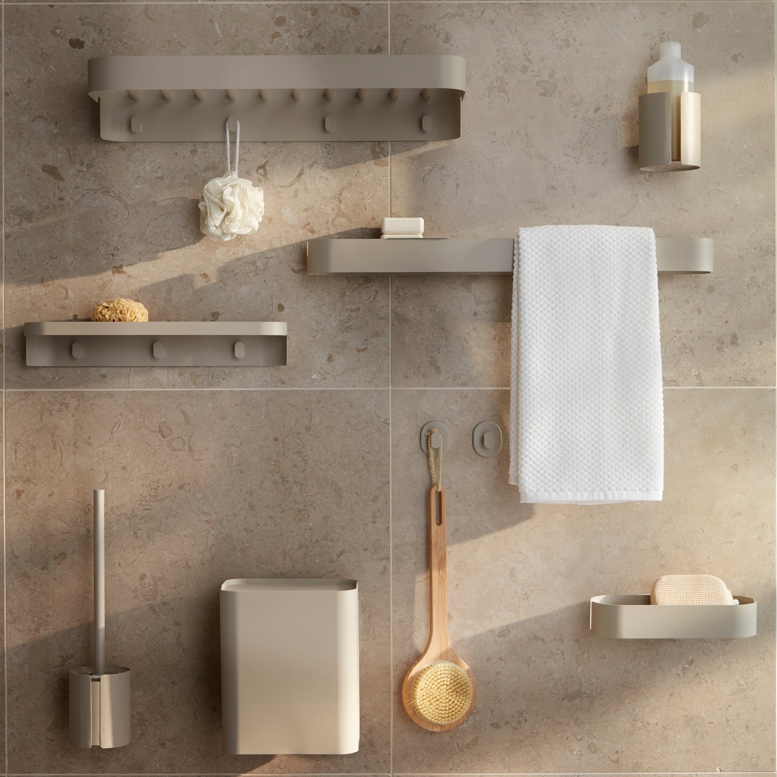 Multiple grey-beige FLORSJÖN bathroom storage accessories including a towel rail, waste bin and hooks are on a tiled wall.