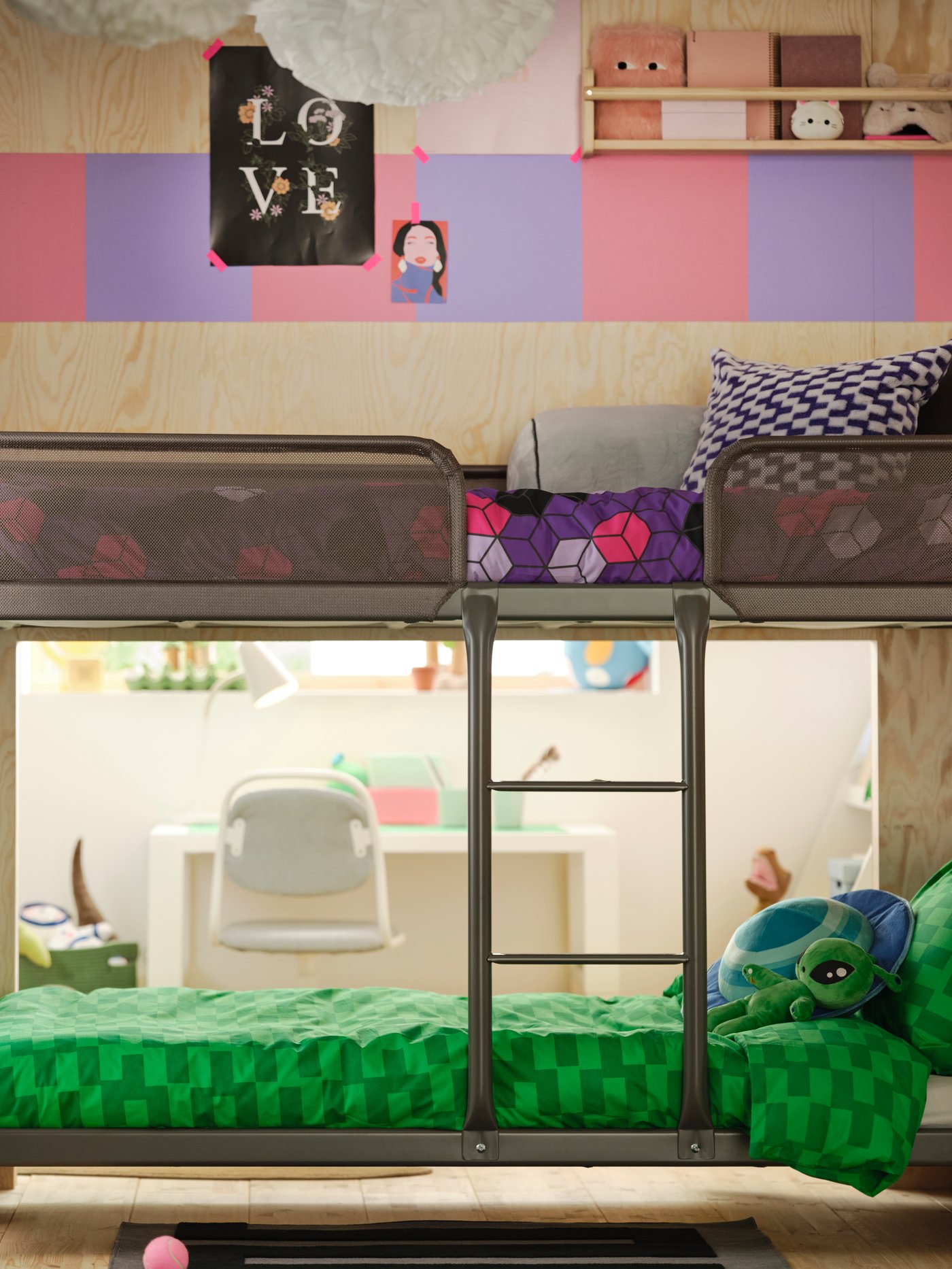 Es sind ein TUFFING Etagenbettgestell und der dahinter liegende Raum zu sehen. Das untere Bett ist mit grüner Bettwäsche, das obere mit lilafarbener Bettwäsche bezogen.