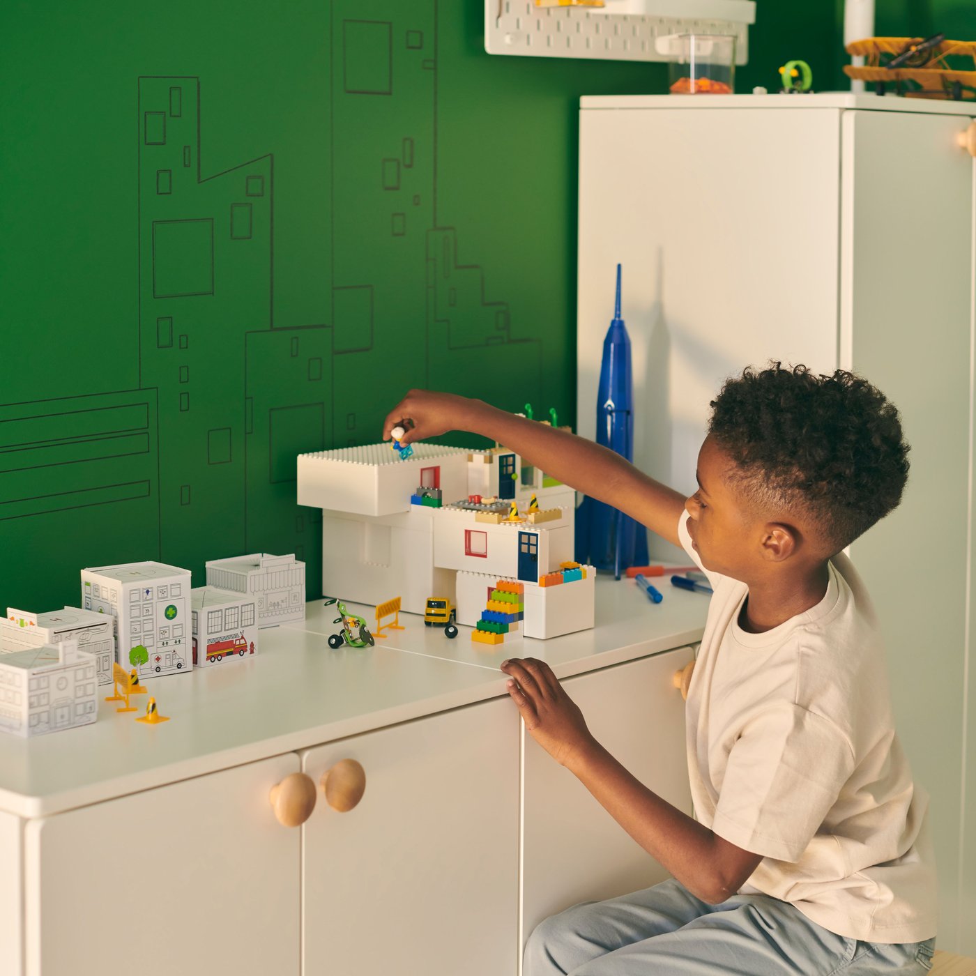 Ein Kind sitzt auf einem Hocker und spielt mit BYGGLEK LEGO Bausteinen auf einer SMÅSTAD Kleiderschrankkombination.