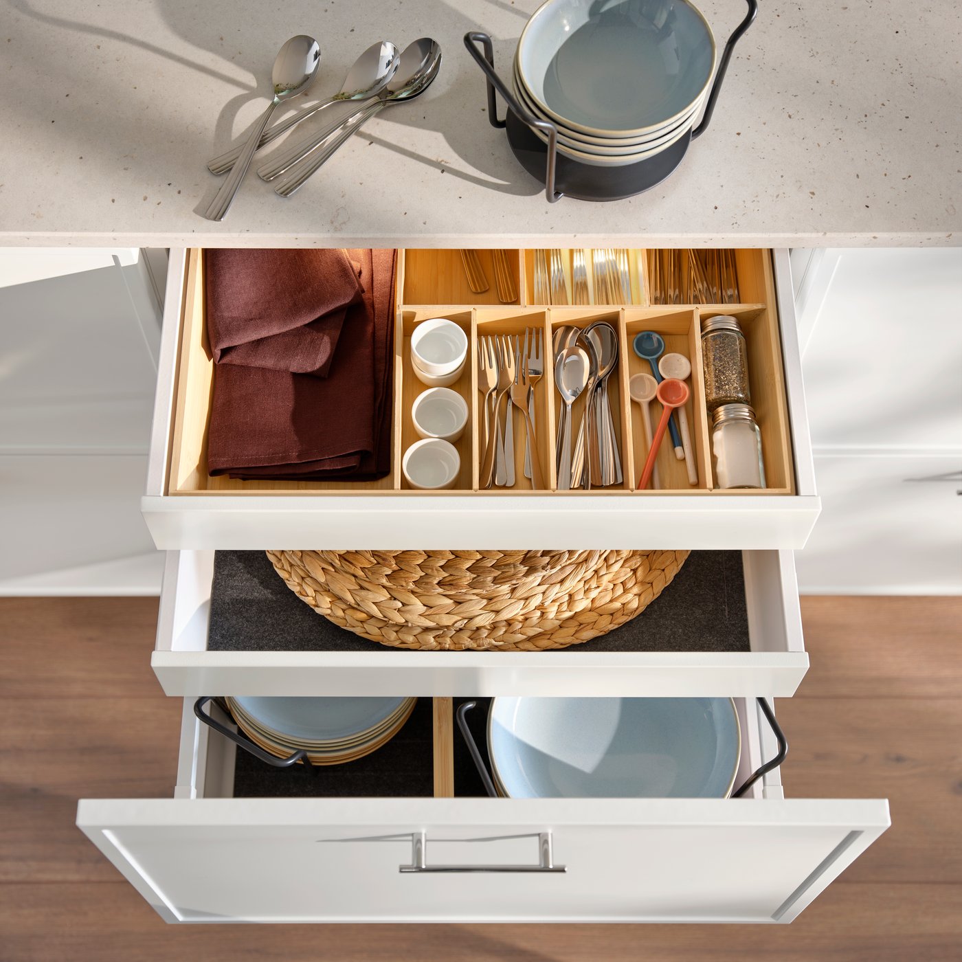 An opened  kitchen drawer with a light bamboo UPPDATERA cutlery tray containing utensils, spice jars and a small textile.