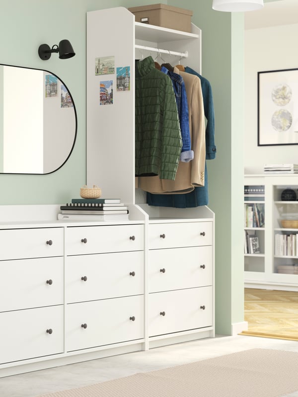 Hallway with wide, white HAUGA chest and wardrobe combo. In the adjacent living room stands a white HAUGA glass-door cabinet.