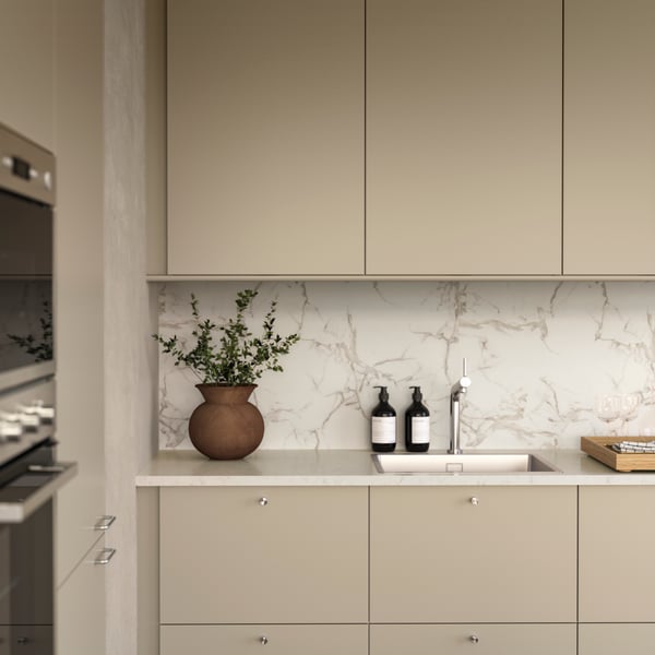Ett ljust, modernt kök har eleganta, beige HAVSTORP luckor och fronter med knoppar i rostfritt stål och en diskho i rostfritt stål.
