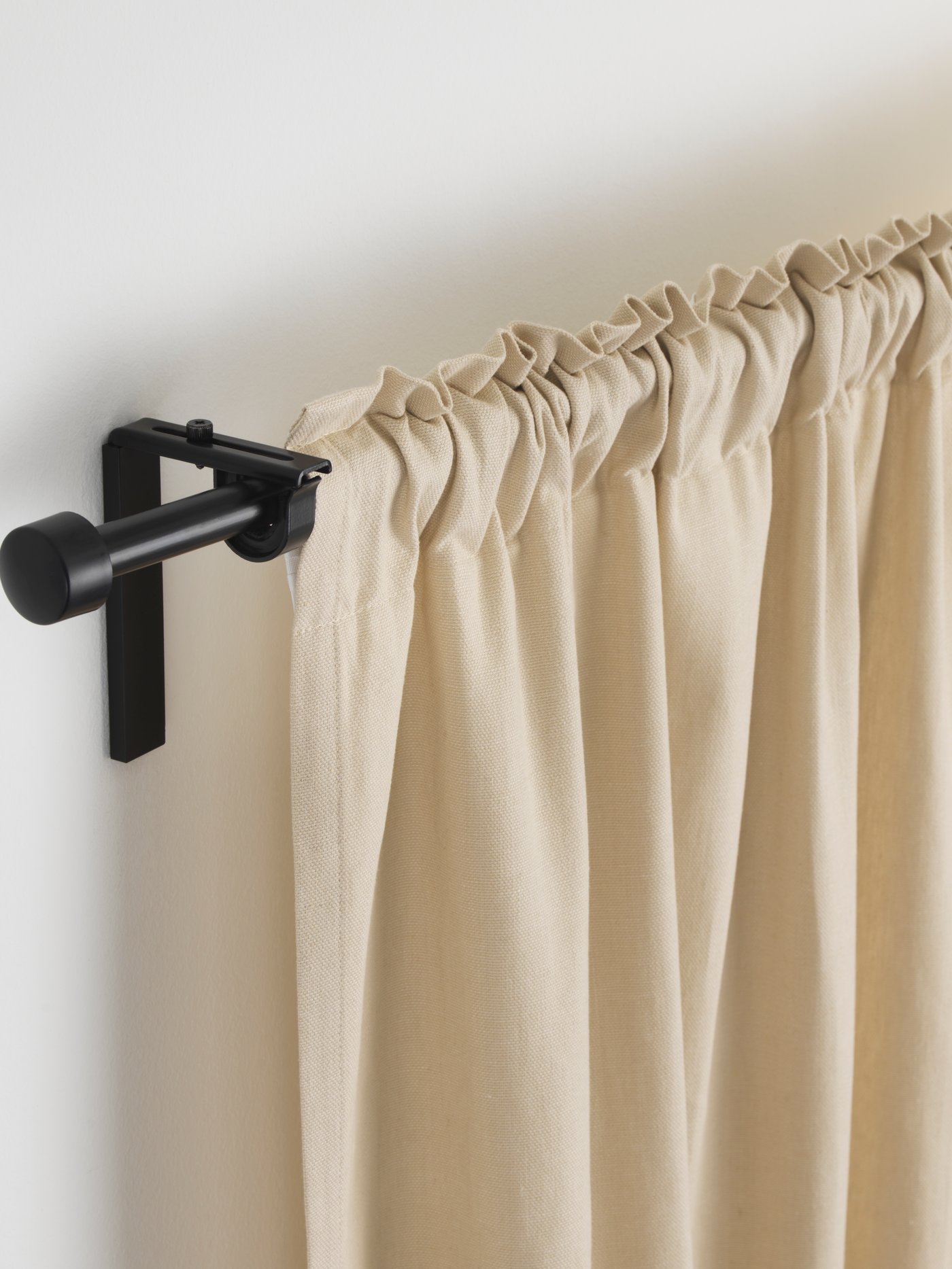 A black RÄCKA curtain rod set with a beige curtain hanging from it.