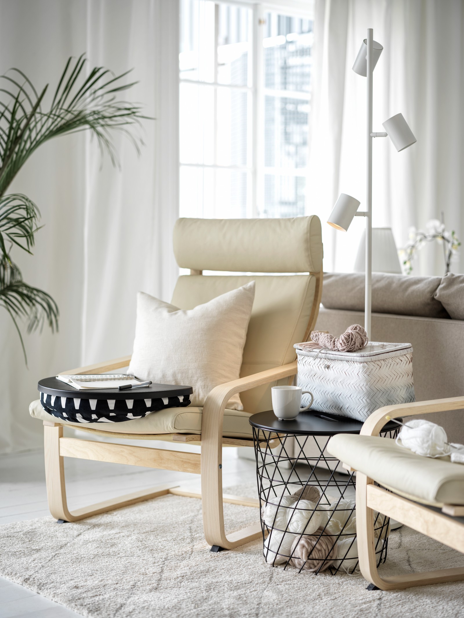 Dve krem fotelje s podnožjem u retro stilu u beloj dnevnoj sobi u skandinavskom deko stilu s crnim stočićem za kafu s odlaganjem i sivim tepihom s niskim florom ispod.