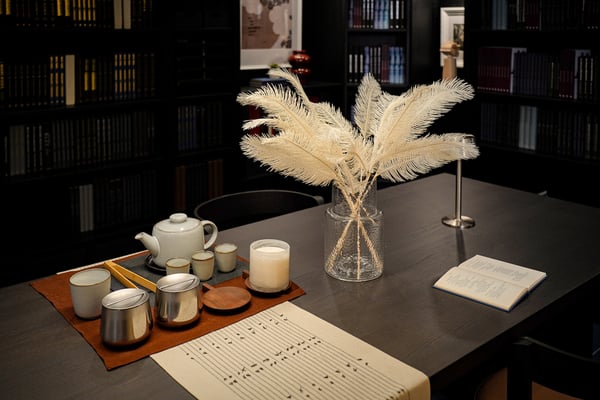 Dark brown BERGSHYTTAN dining table featuring an in/outdoor/beige SMYCKA artificial spray in KONSTFULL vase, VARARV table runner, GLADELIG tea pot and AFTONHAJ jar.