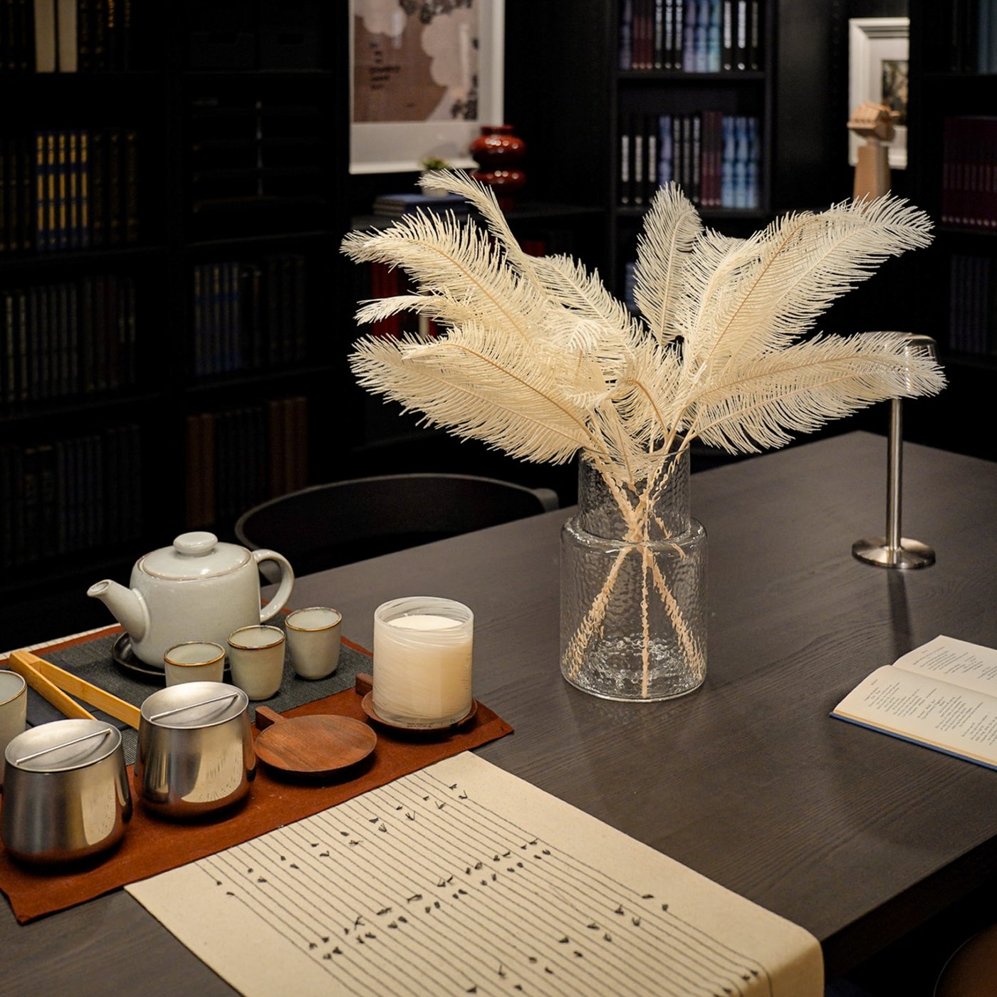 Curious Library room setting at IKEA Tampines, featuring a dark brown BERGSHYTTAN dining table. A KONSTFULL vase, a GLADELIG teapot and GLADELIG teacups and stainless steel AFTONHAJ jar with lids on top of a VÅRARV table-runner.