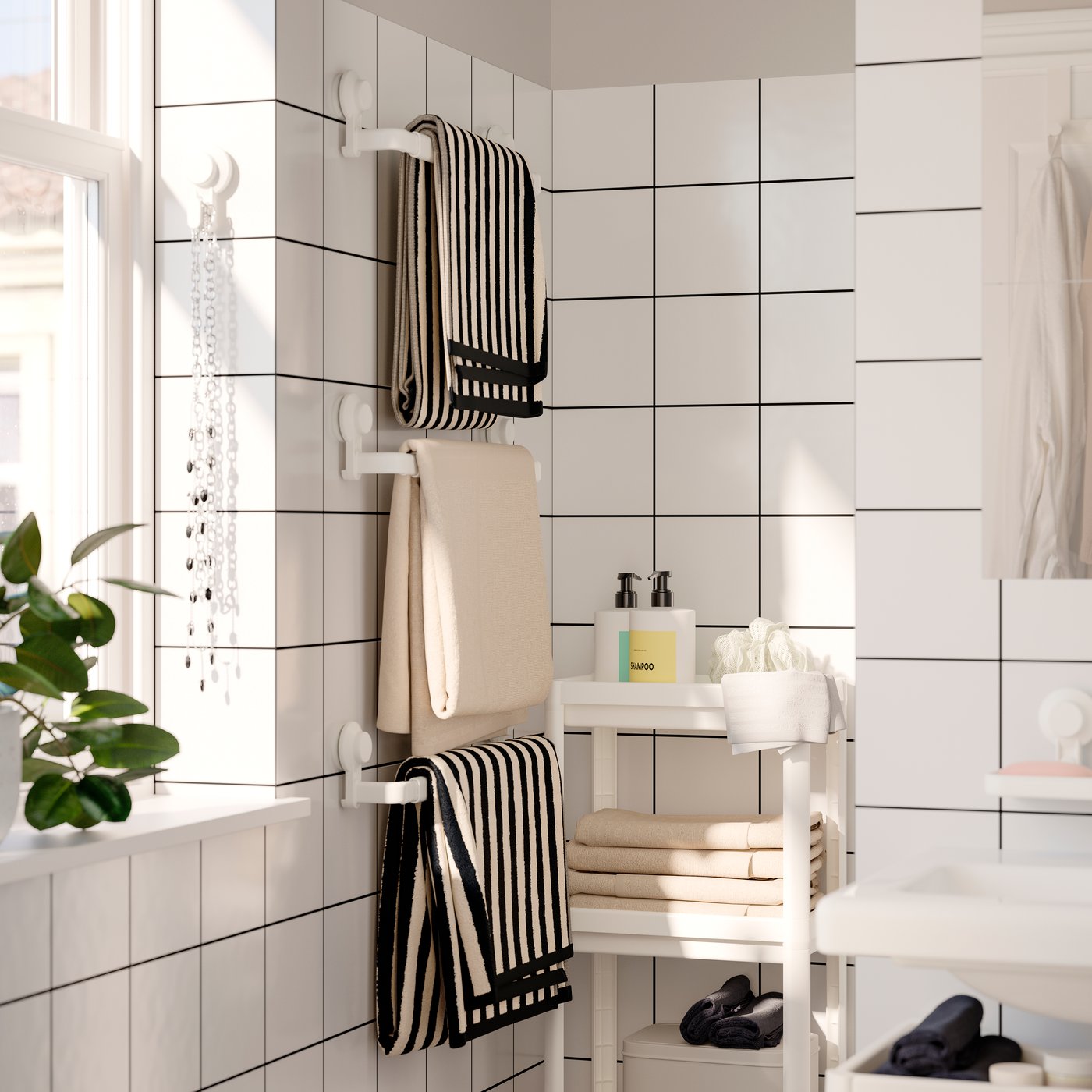 Three bath towels in beige and black-and-white stripes hanging on three TISKEN towel racks with suction cup. White tiles.