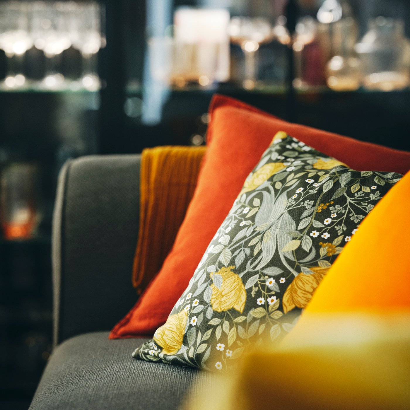 A sofa with a cushion in a red-brown DYTÅG cushion cover and cushion in a deep green/floral pattern TUVSÄV cushion cover.