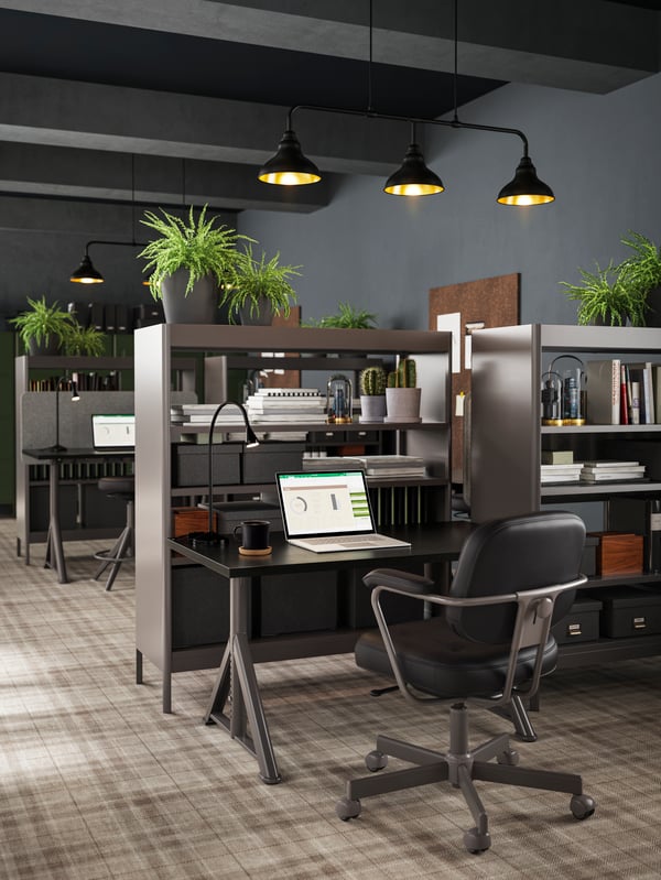 مكتب أسود/رمادي داكن وكرسي من الجلد الأسود مع رف مدمج ومقسم للغرفة معروض بجوار عدة مكاتب.