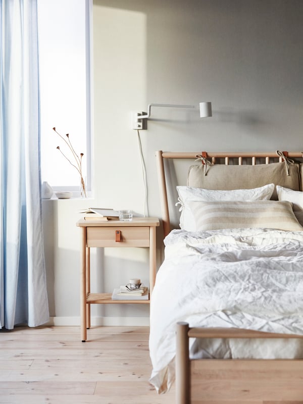 Een houten bed en nachtkastje in een lichte slaapkamer met houten vloer en blauw gordijn