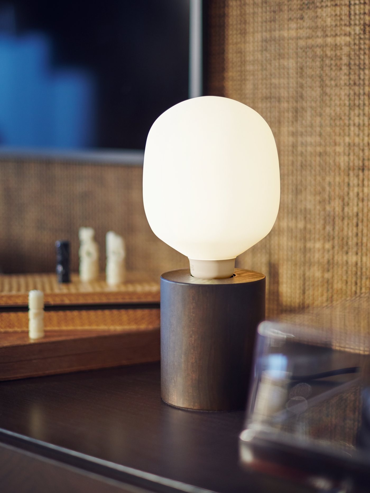 A dark brown wood BLEKKLINT table lamp finished with a TRÅDFRI LED dimmable white frosted glass bulb.