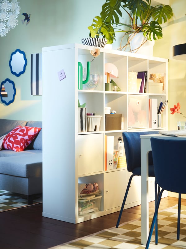 A KALLAX shelving unit filled with storage and decoration acts as a room divider between a dining area and a living room.