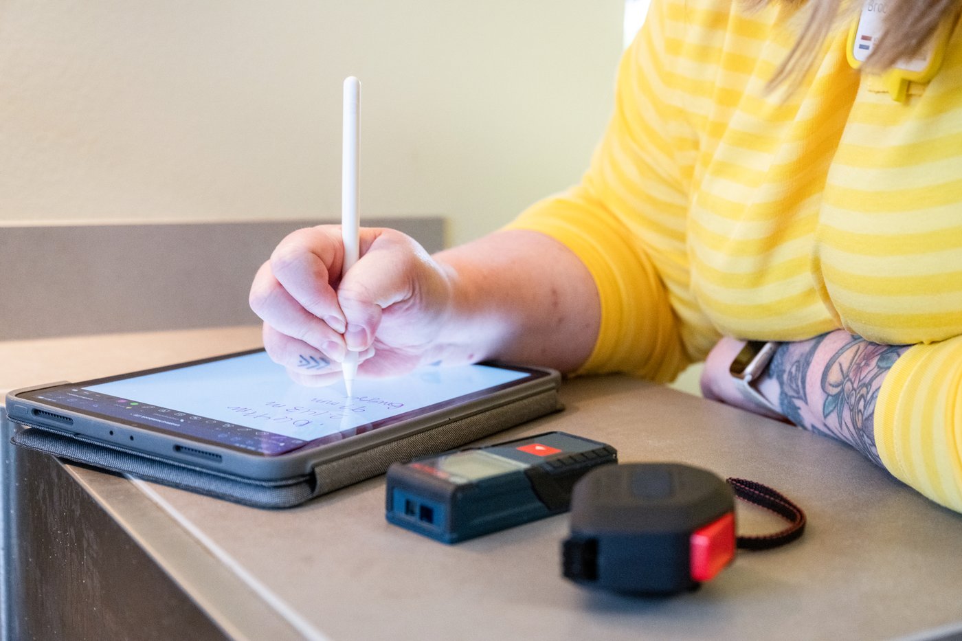 Pracowniczka IKEA notująca wymiary kuchni na ekranie tabletu. Obok tabletu, na blacie kuchennym, leży miarka i dalmierz.