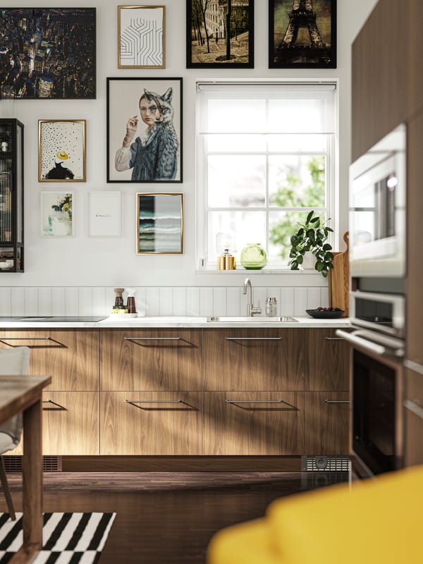 A kitchen with TISTORP fronts with a brown walnut effect, a dark wood floor and some posters on the wall next to a window.