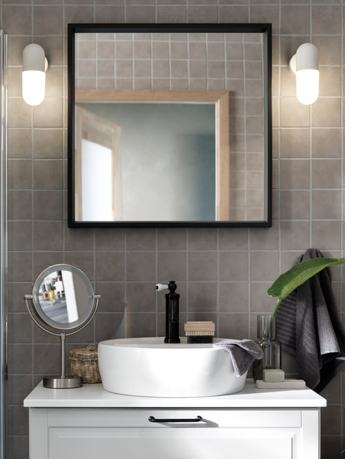 Front shot of a white countertop wash basin with a black mixer tap, on a wash stand with drawers. A mirror is on the wall.
