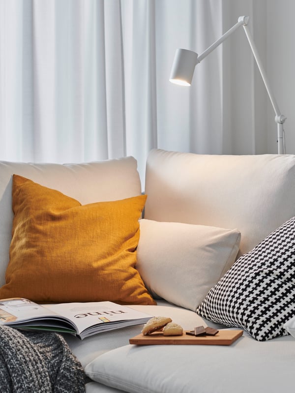 I ett mysigt vardagsrum sitter en man i en soffa och läser en bok. En golvlampa ger bra läsbelysning.
