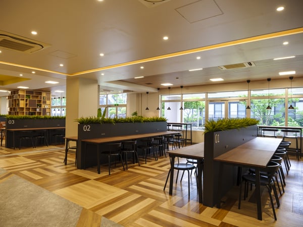 複数のテーブルと椅子が配置されたオープンスペース。プランターで区切られた緑豊かな空間