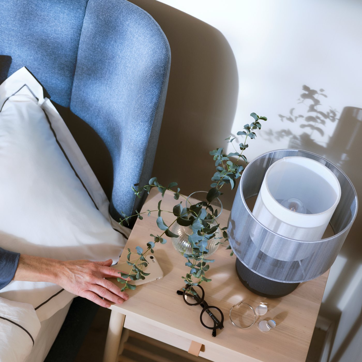 En man och en kvinna ligger i sängen, i förgrunden står en lampa och i bakgrunden syns ett fönster med en halvt neddragen rullgardin.