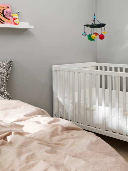 Kinderzimmer mit Bettgestell, Kissenbezug, Babybett, Bettwäsche, Kinderspielzeug, Bettwäsche, Wandregal und Büchern.