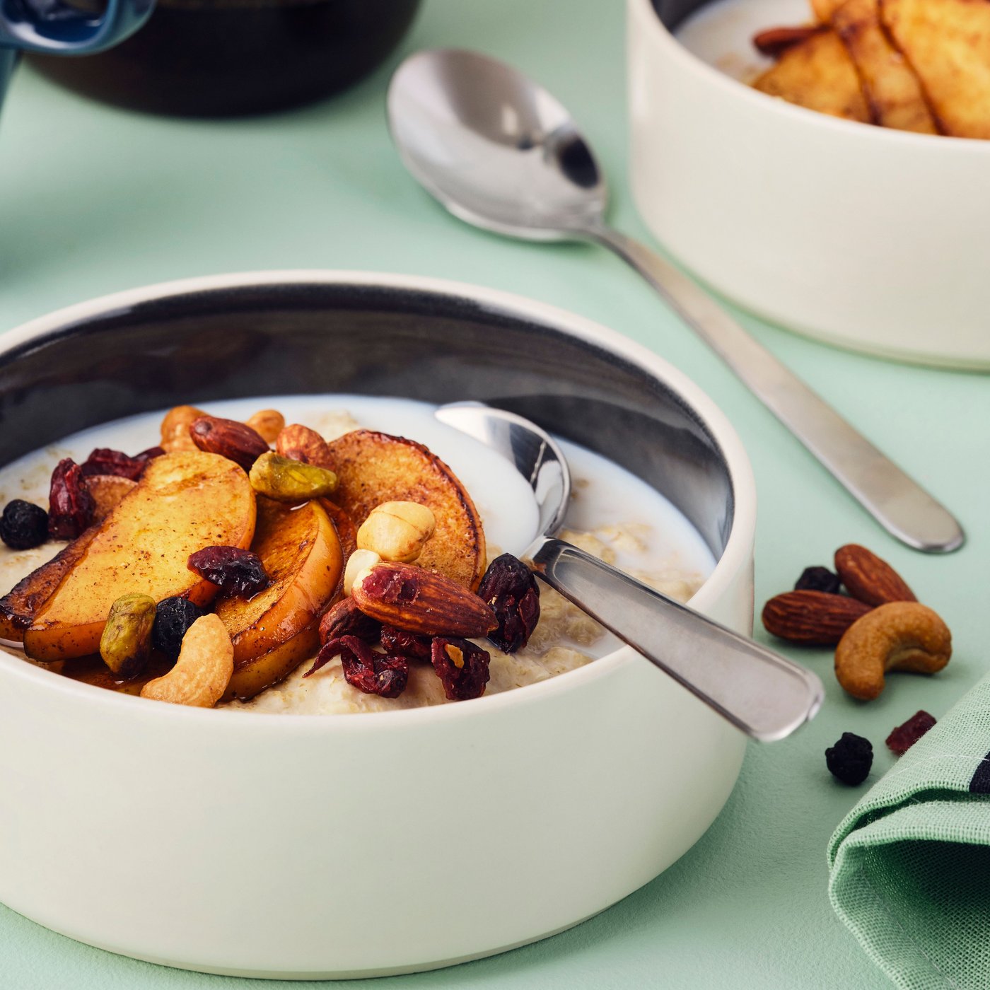 A bowl of porridge topped with cinnamon-fried apples and MUNSBIT mix roast nuts/berries on a green tablecloth.