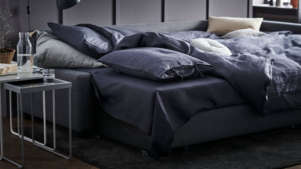A dark grey FRIHETEN KLAGSHAMN sofa-bed with storage in the bedroom.
