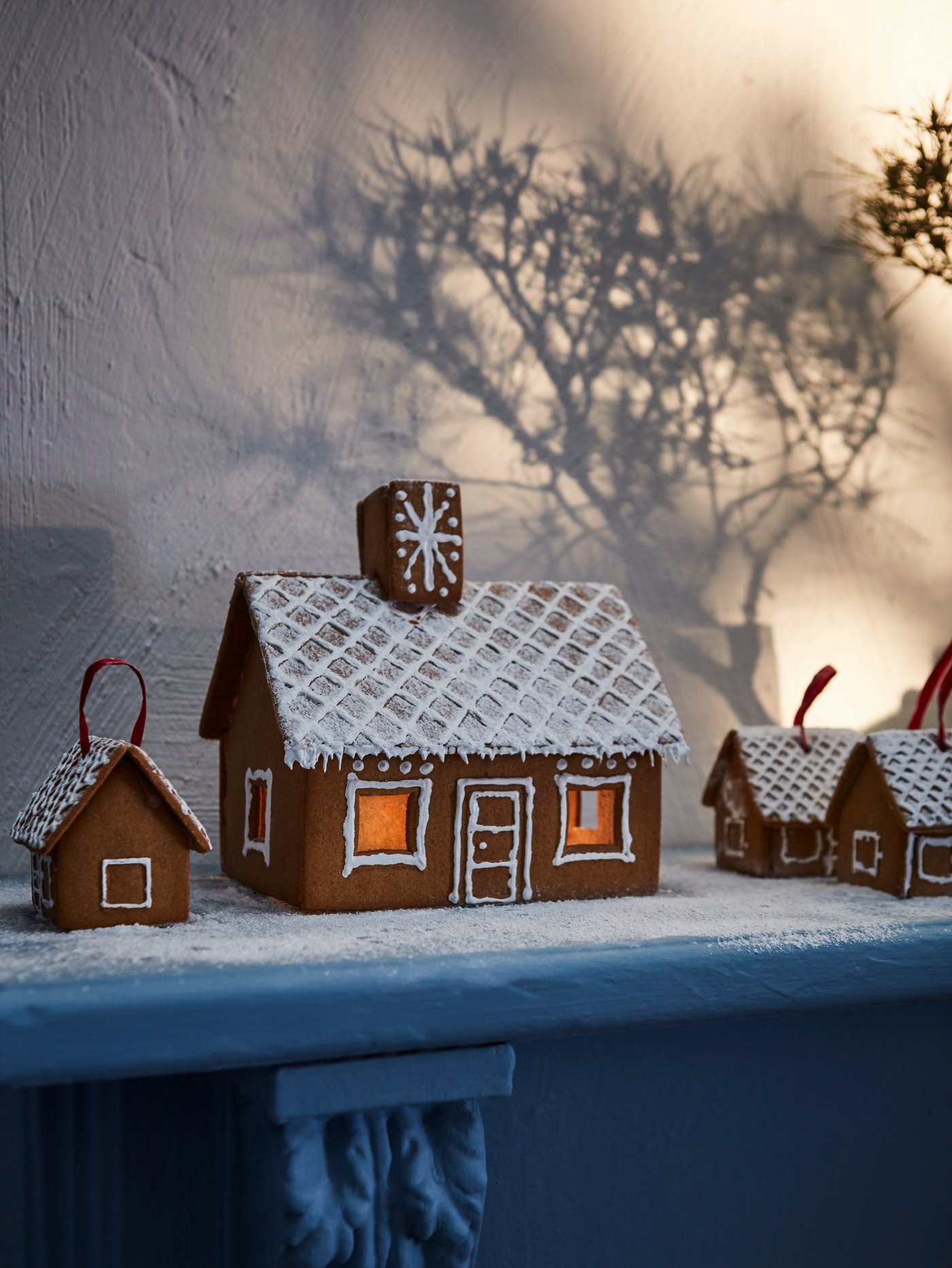 A VINTERSAGA gingerbread house and mini gingerbread houses set on artificial snow decorate a grey mantelpiece.