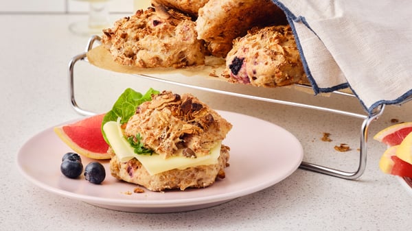 A granola breakfast bun with cheese and lettuce is placed on a pink plate with some blueberries and a slice of grapefruit.