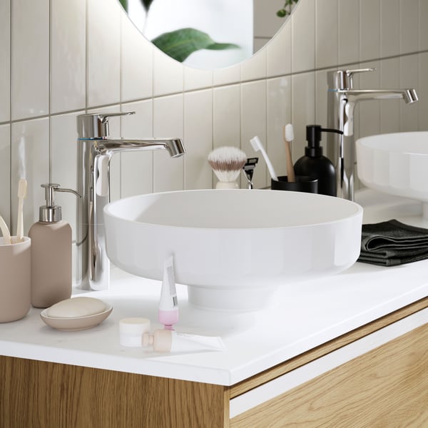 Ein modernes Badezimmer mit LERSJÖN Waschtisch, Chromarmaturen und stilvollen Accessoires auf einem Waschtischunterschrank aus Holz.
