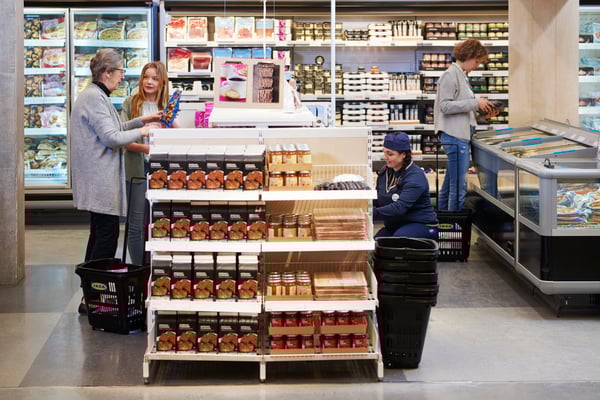 Tre kunder och en IKEA medarbetare befinner sig i matbutiken i ett varuhus. På en gavel exponeras skärbrädor tillsammans med matprodukter från IKEA.
