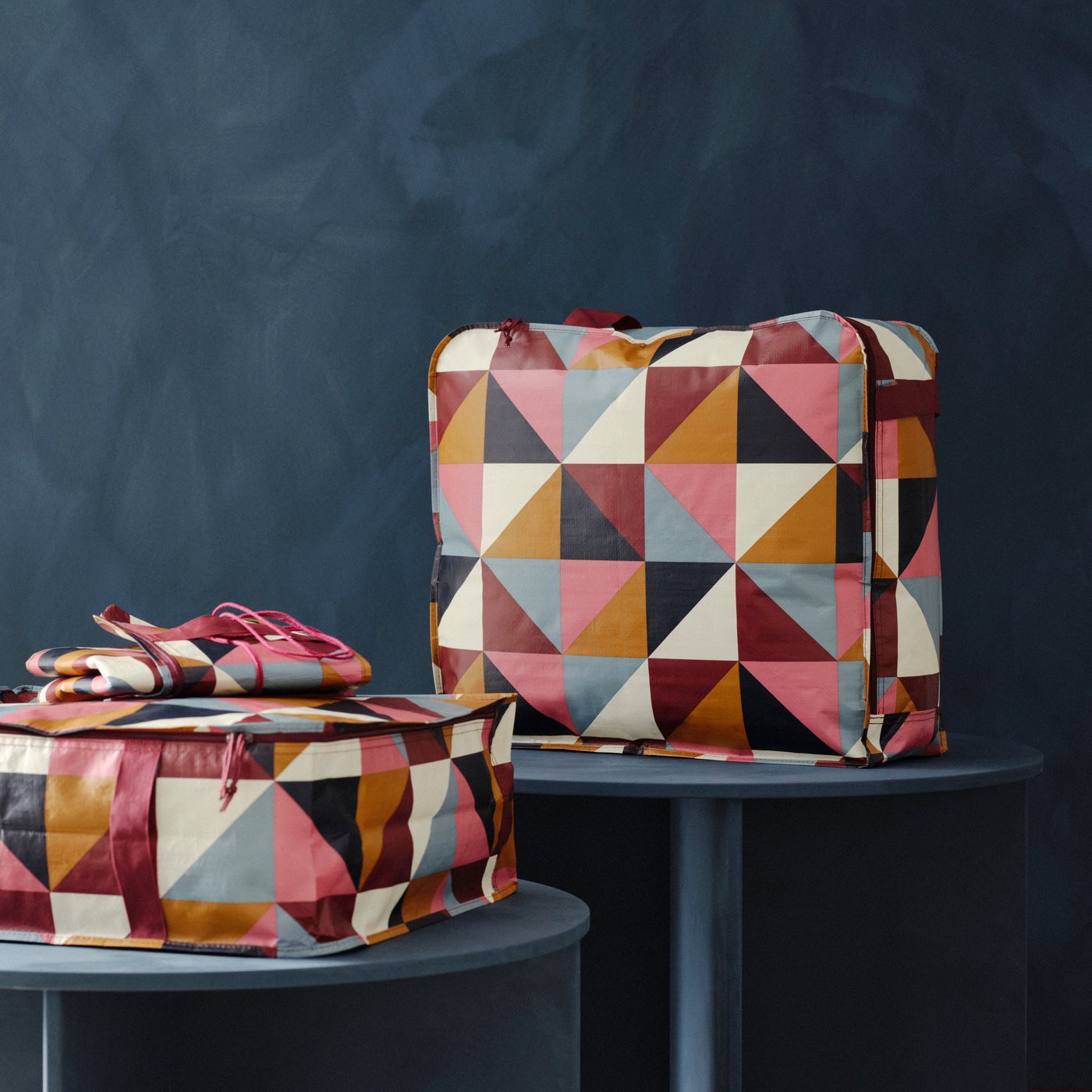 Dua bekas storan SÄCKKÄRRA dan satu bekas tidak berlipat yang sepadan terletak di atas meja bulat berwarna biru di ruang studio berwarna biru.